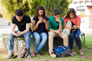 Group of teenage boys and girls ignoring each other while using their cell phones at school